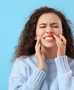 pained woman touching her sensitive gums on a blue background