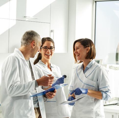 Three dental staff members talking and holding clipboards