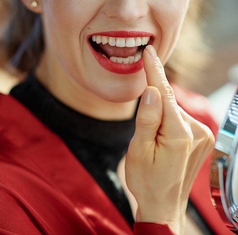 Closeup of smiling patient pointing to flawless tooth that has tooth bonding on it