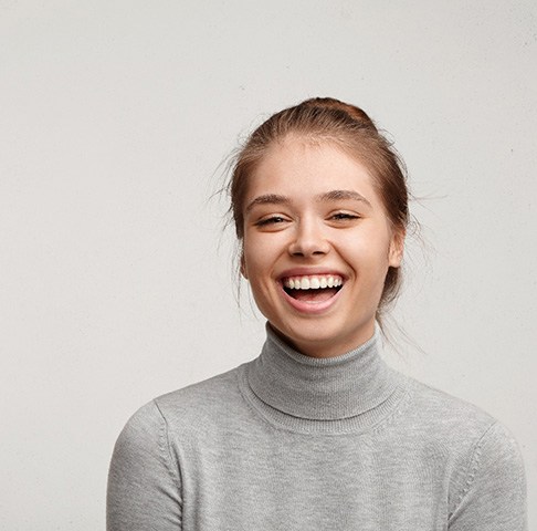 Woman in gray sweater with beautiful teeth smiles confidently after getting tooth bonding 