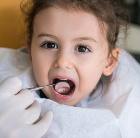 Dentist examining child's smile after tooth colored filling restoration