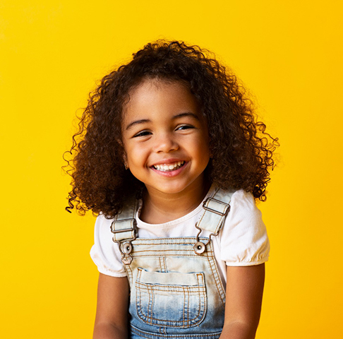 Cute little girl on yellow background smiling after visiting the dentist 