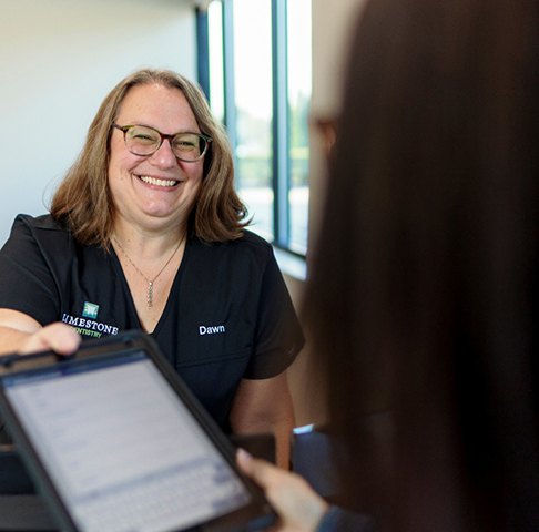 Smiling receptionist handing patient a tablet with dental insurance paperwork