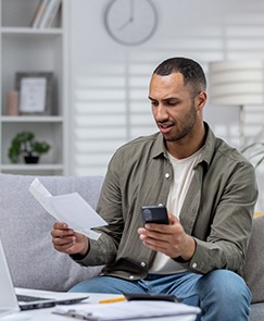 man sitting in front of laptop holding insurance paperwork and cell phone