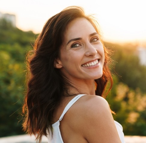Woman looking over her shoulder and smiling outside during sunset
