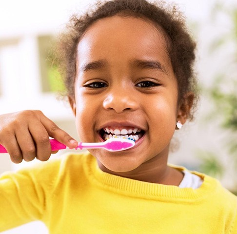 Closeup of young girl in a yellow shirt brushing her teeth with fluoridated toothpaste