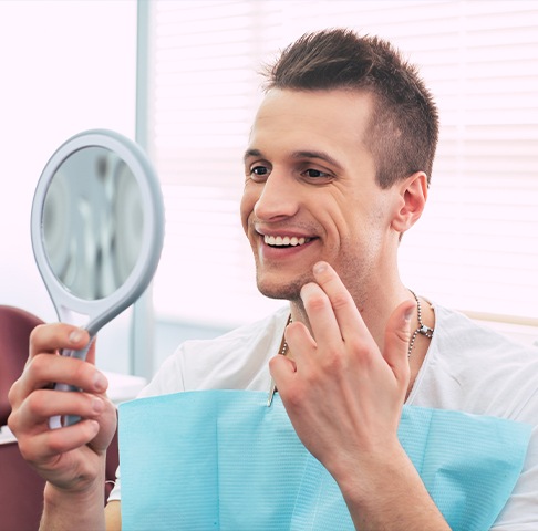 Man looking at smile in mirror during first dental appointment