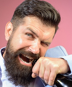 Man with beard and suit biting a bottle top on pink background