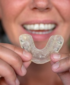 Closeup of a mouthguard being held out by a patient with dental implants 