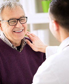 Older man with dental implants smiling at his dentist