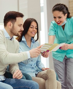 Patients smiling and reviewing dental insurance paperwork with dental hygienist