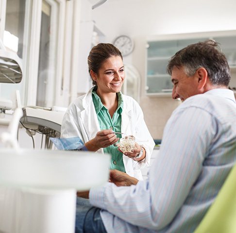 Smiling dentist showing patient model of teeth