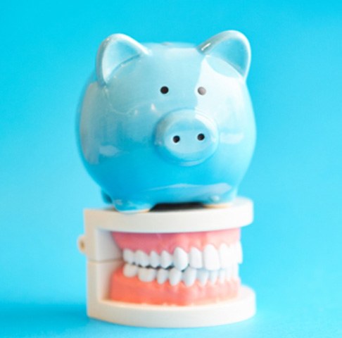 Blue piggy bank atop set of model teeth on a blue background