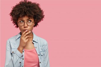 Woman with glasses on pink background wondering about cosmetic dentistry
