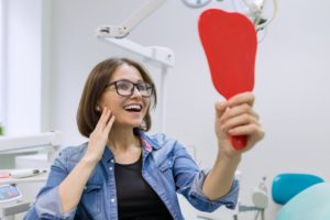 Woman admiring her smile in a mirror after cosmetic dentistry