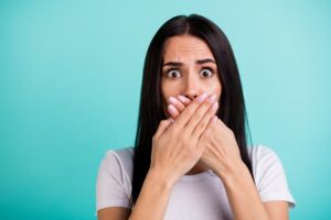 Surprised and worried woman covering her mouth on blue background